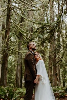 a bride and groom standing together in the woods