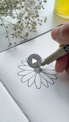 someone is drawing a flower on paper with a marker