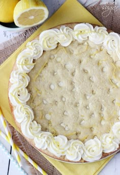 a pie with white frosting and lemons next to it on a yellow napkin