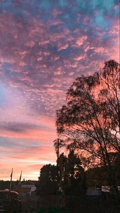 the sky is pink and blue as the sun sets in the distance with trees silhouetted against it