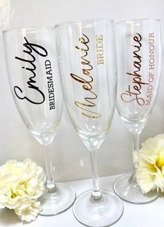 three wine glasses with the names of bride and groom on them sitting next to flowers