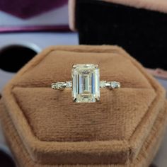 an emerald cut diamond ring sitting on top of a velvet box