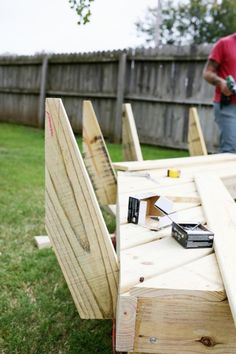 a man standing next to a wooden table with tools on it in the grass near a fence