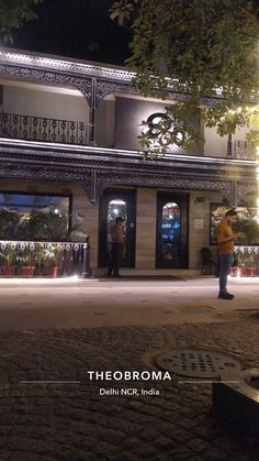 two people standing in front of a building at night with lights shining on the windows