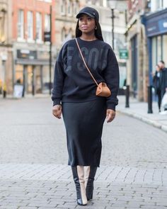 a woman walking down the street wearing a black sweatshirt and skirt