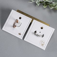 two pairs of earrings sitting on top of a white box next to a green plant