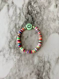 a bracelet with a smiley face and multicolored beads on top of a marble surface