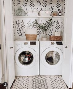 a white washer and dryer sitting in a room next to a wall with leaves on it