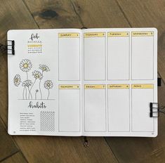 an open planner with yellow stickers on it and flowers in the pages, sitting on a wooden floor