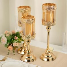 two gold candlesticks sitting on top of a table next to plates and flowers