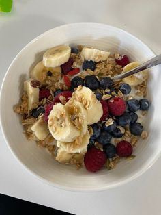 a white bowl filled with granola, berries and bananas on top of a table