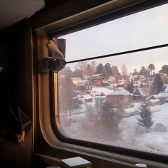 a view from the inside of a train looking out at snow covered houses and trees