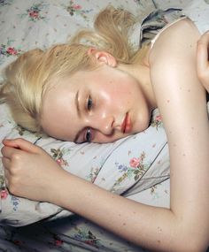 a young blonde woman laying in bed with her eyes closed