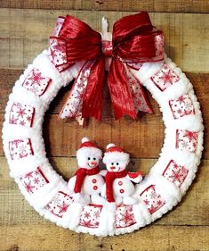 a christmas wreath with two snowmen hanging on the front and one is decorated with red ribbon