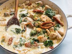 a skillet filled with chicken and spinach covered in white sauce next to a wooden spoon