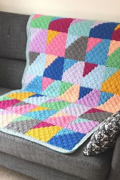 a crocheted blanket sitting on top of a gray couch next to a pillow