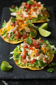 three tortillas topped with chicken, lettuce and tomatoes on a black tray