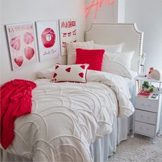 a white bed with red pillows and pictures on the wall