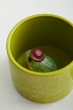 a small green frog in a yellow cup with a red hat on it's head