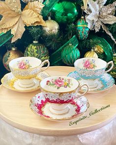 three tea cups and saucers sitting on top of a wooden table next to a christmas tree