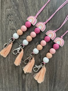 four different colored beads and tassels on a wooden table with pink, white, orange