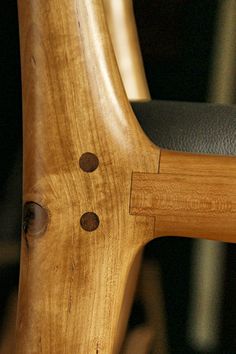 a wooden chair with black leather upholstered seat and armrests that have holes in the wood