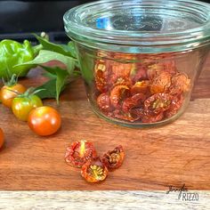 tomatoes and other vegetables on a wooden cutting board next to a glass jar with red peppers in it