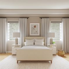 a large white bed sitting in a bedroom next to two windows with curtains on them