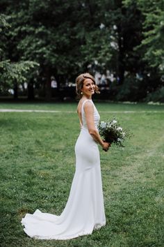 a woman in a white dress is holding a bouquet and smiling at the camera while standing on some grass