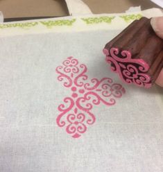 a stamper being used to make an intricate design on a piece of fabric with pink ink