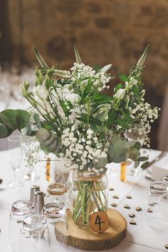 a vase filled with white flowers sitting on top of a wooden table next to wine glasses