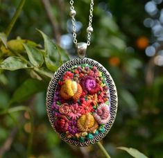 a close up of a necklace on a chain with flowers in the center and leaves around it