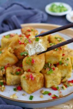 chopsticks picking up some fried food on a white plate with green and red sprinkles