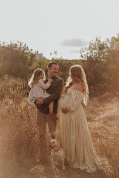 a man, woman and child standing in tall grass with a dog