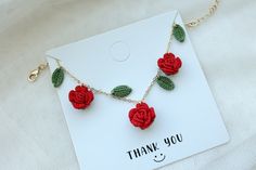 a red rose necklace with green leaves attached to it on a card that says thank you