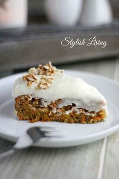 a white plate topped with a piece of cake covered in frosting and nuts next to a fork