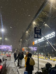 people are standing on the side walk in the snow near a bus stop at night