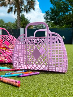 two pink baskets and some colored crayons on the grass with palm trees in the background