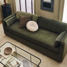 a living room with a green couch and glass coffee table in front of the window