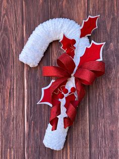 a white wreath with red ribbon and holly leaves on it sitting on top of a wooden table