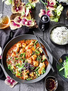 a bowl filled with food next to rice and other dishes on a table, surrounded by orchids