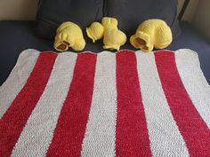 three yellow stuffed animals sitting on top of a red and white striped blanket in front of a black couch