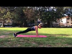 a woman is doing push ups on a pink mat in the middle of a park