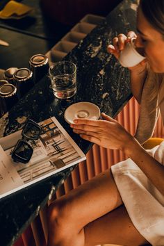 a woman sitting at a table drinking from a cup