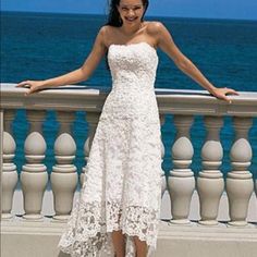 a woman in a white dress standing on a balcony next to the ocean with her arms outstretched