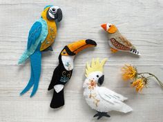 three colorful birds sitting on top of a wooden table next to plants and flowers in vases