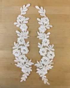 two white flowers and leaves are on a wooden surface, one is made out of lace