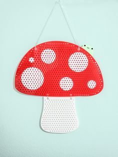 a red mushroom with white dots hanging from a hook on a wall in front of a light blue background