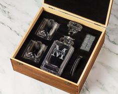 an open wooden box with four glass bottles in it on a marble counter top next to silver objects