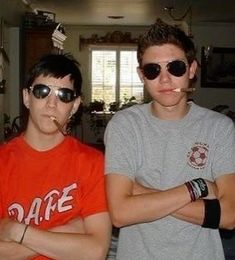 two young men standing next to each other with their arms crossed and one man wearing sunglasses